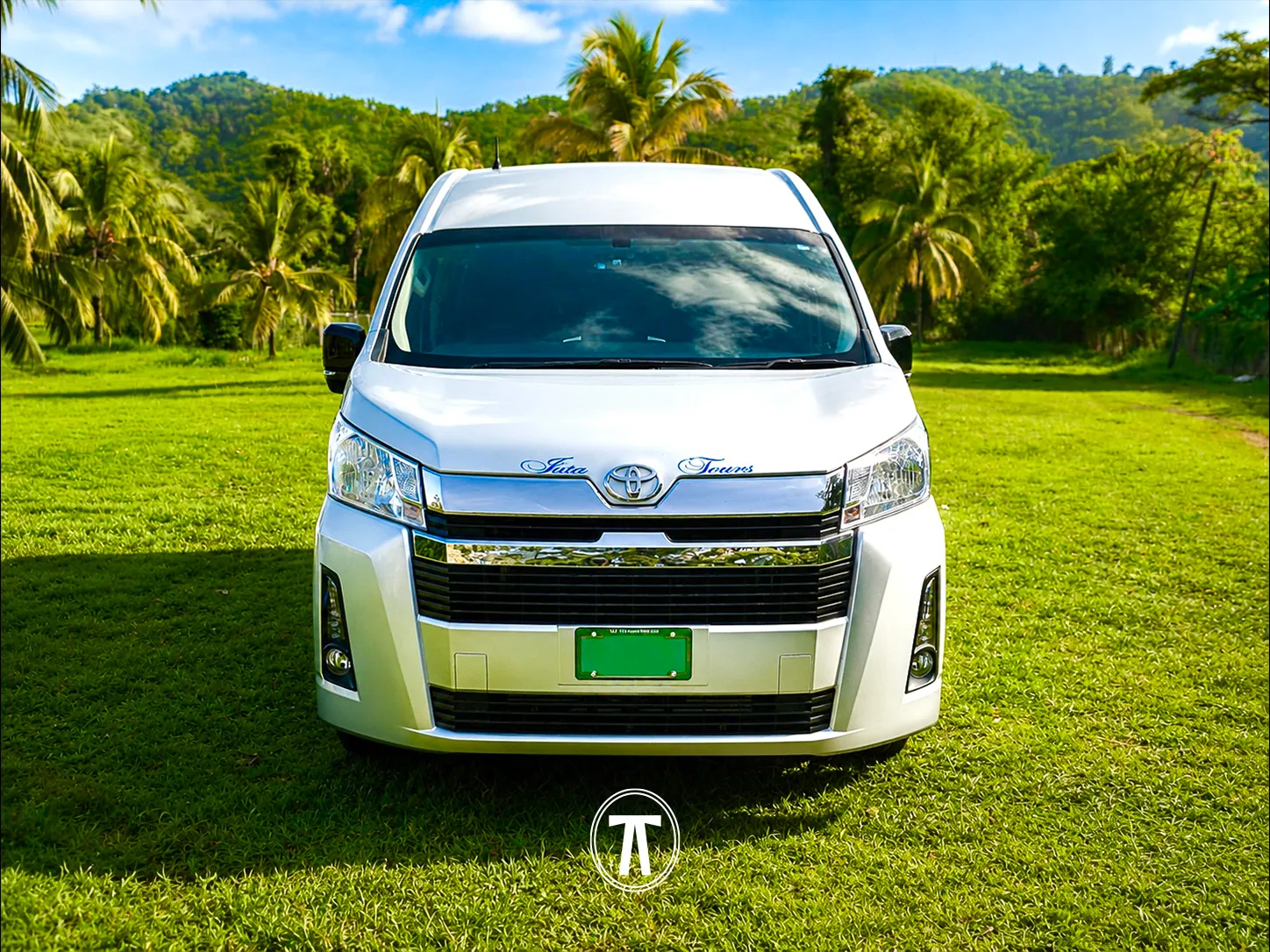 Silver passenger van with Juta Tours branding, parked among palm trees